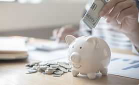 Hand putting $100 bill into piggy bank with coins