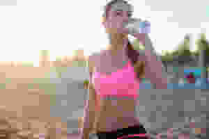 A girl on the beach on a run drinking water.