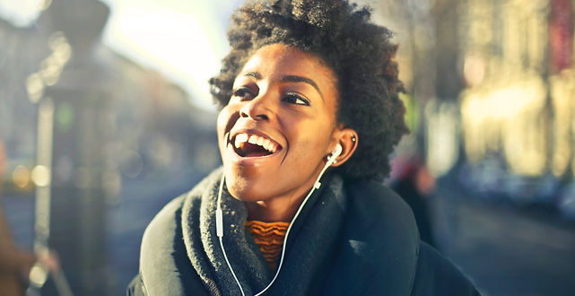 Young black woman with afro listening to music with white earbuds.