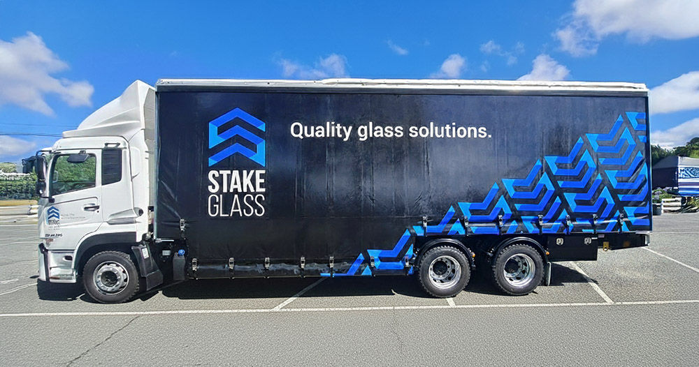 Glass truck driving on a road with a green curtain-side trailer