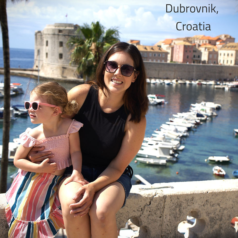 Woman and child in sunglasses enjoying sunny day by Dubrovnik harbor. Historic buildings and boats in the background.