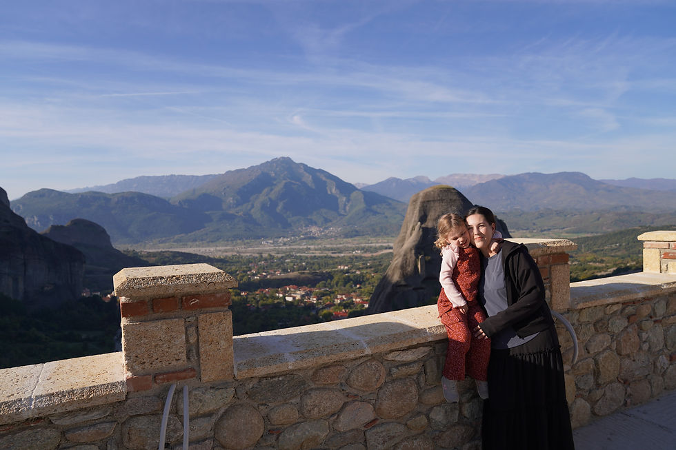Woman and child smiling on a stone terrace with mountains in the background. Clear blue sky. The atmosphere is joyful.