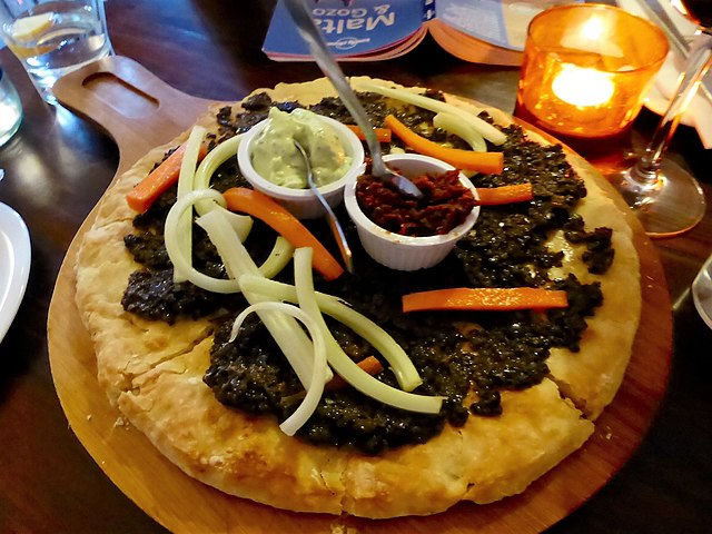Pizza topped with black olives, onion, and red pepper, served with avocado and sun-dried tomato dips. Setting includes candlelight and glass.
