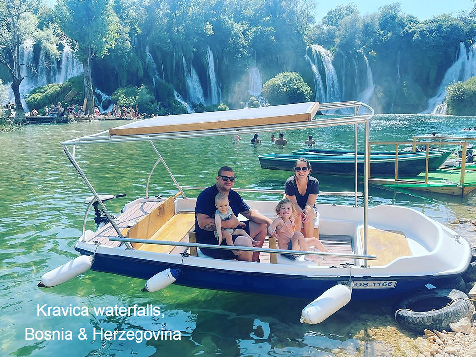 Family on a boat at Kravica waterfalls, Bosnia & Herzegovina. Green water, lush background, and people swimming. Relaxed and sunny mood.