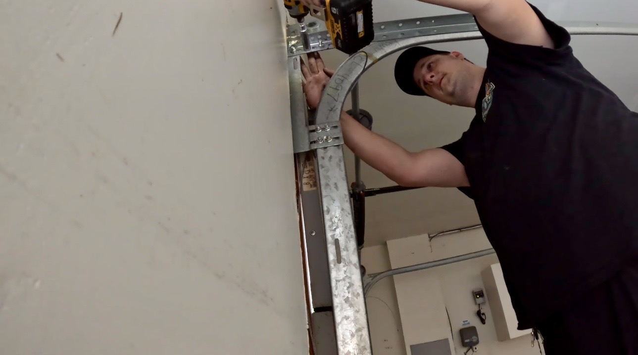 Wesley Zietz using a cordless driver on the upper garage door track bracket.