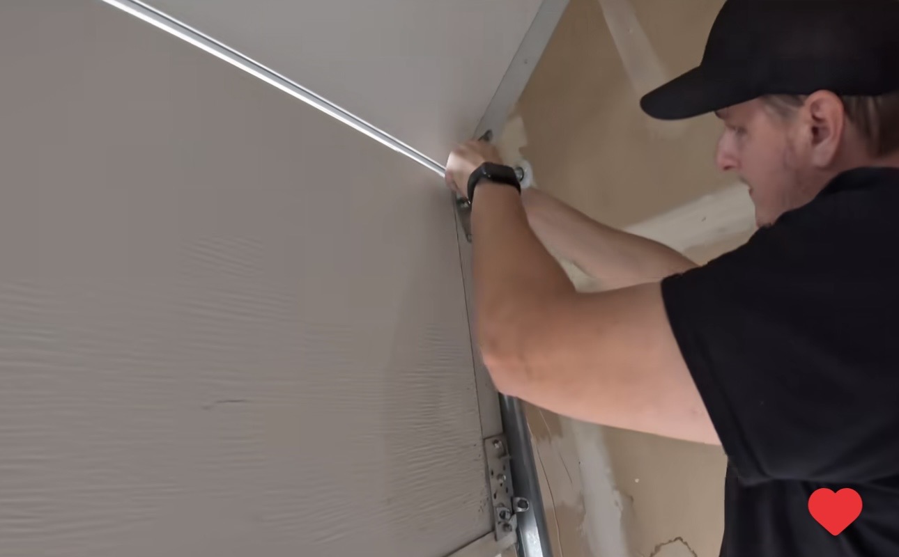 Close-up of Wesley Zietz working on garage door roller and hinge hardware.