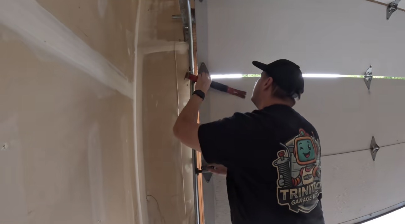 Wesley Zietz using a level beside the vertical garage door track while wearing his Trinitron shirt.