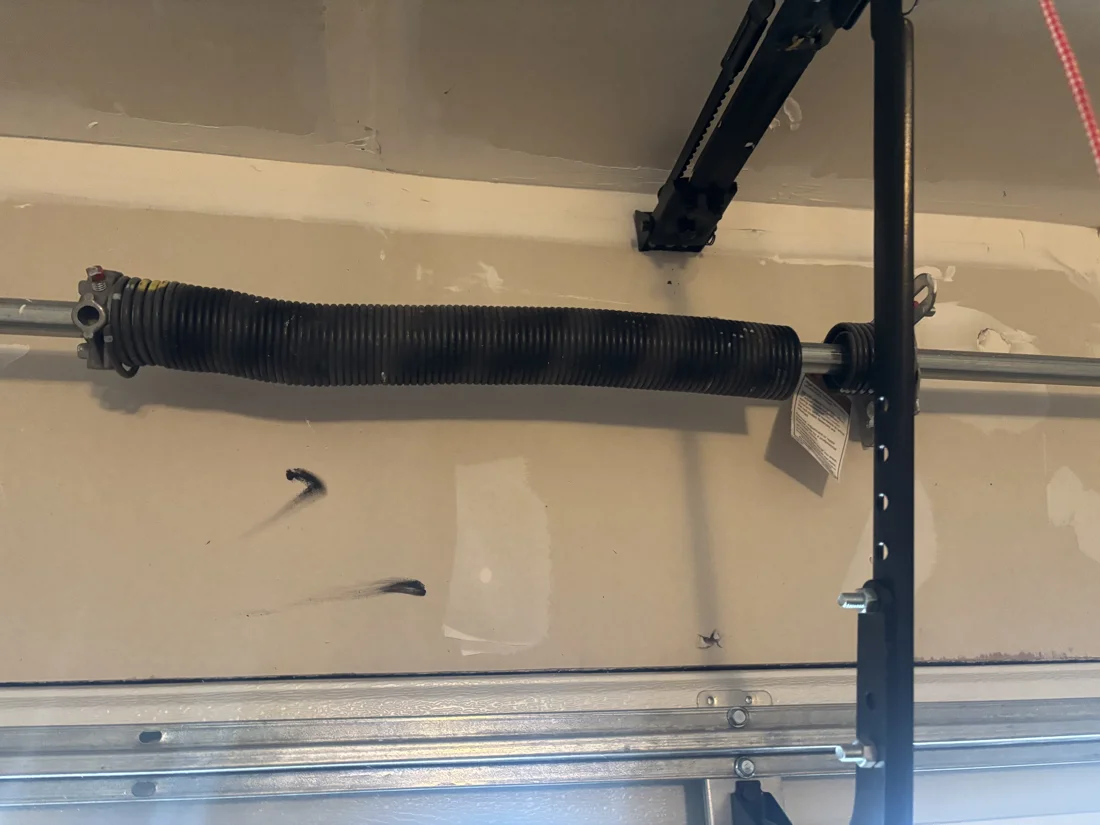 Broken torsion spring with a visible gap near its right end exposing the metal shaft