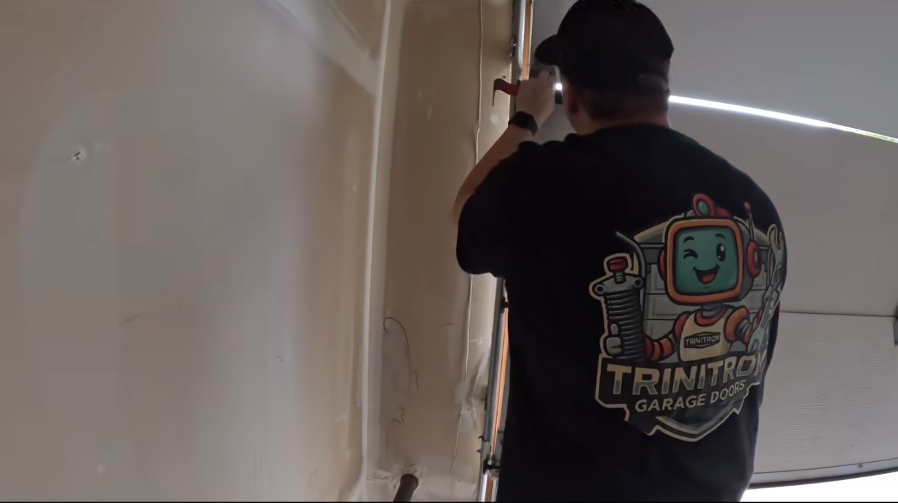 Wesley Zietz working beside the garage door track with the Trinitron Garage Doors logo visible on his shirt.