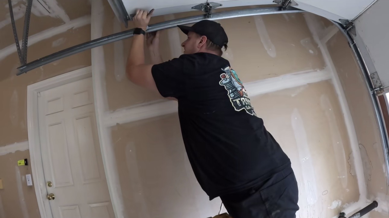 Wesley Zietz working on the overhead garage door track inside a residential garage.