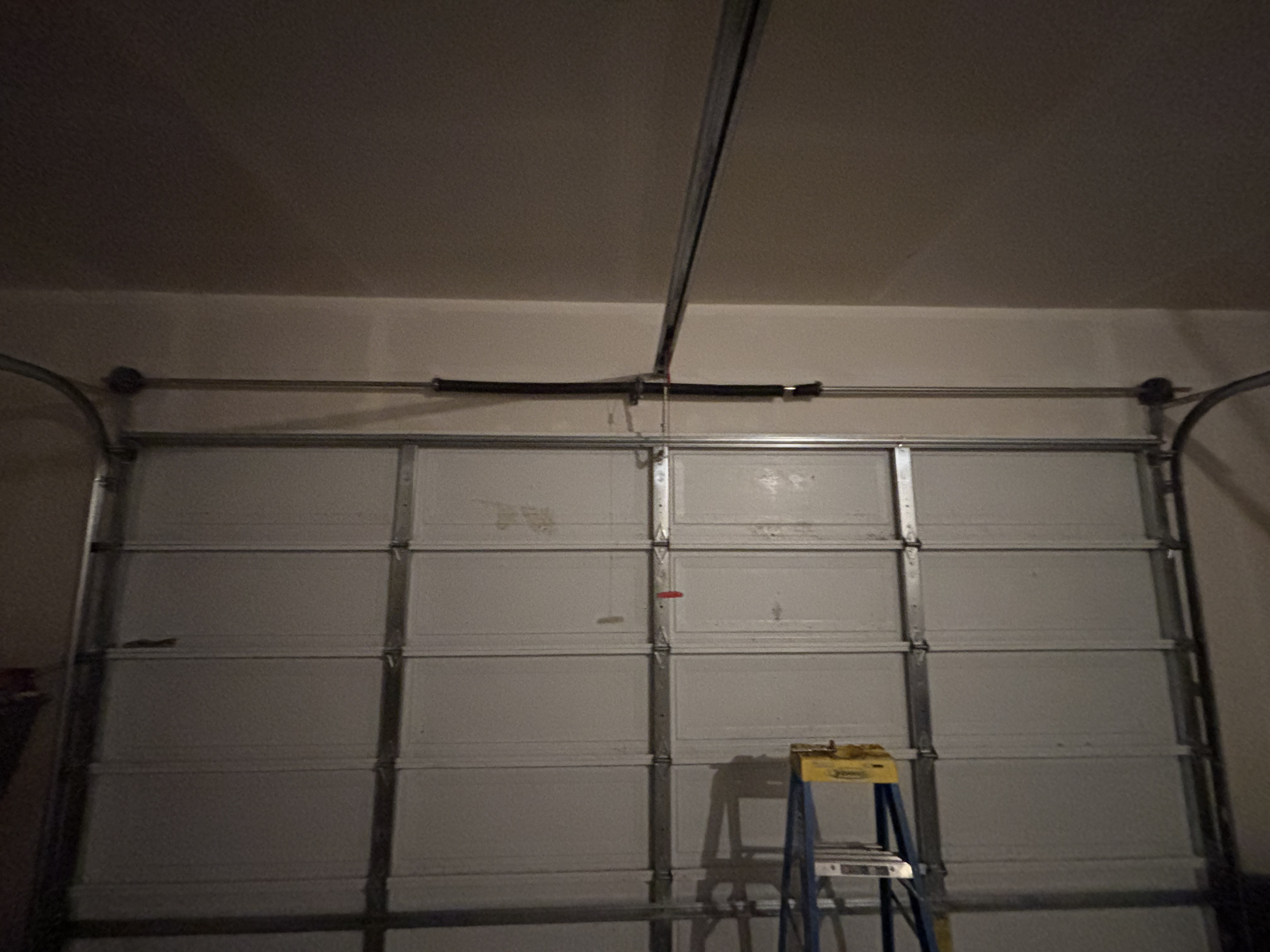 Closed sectional garage door with overhead opener rail and spring shaft