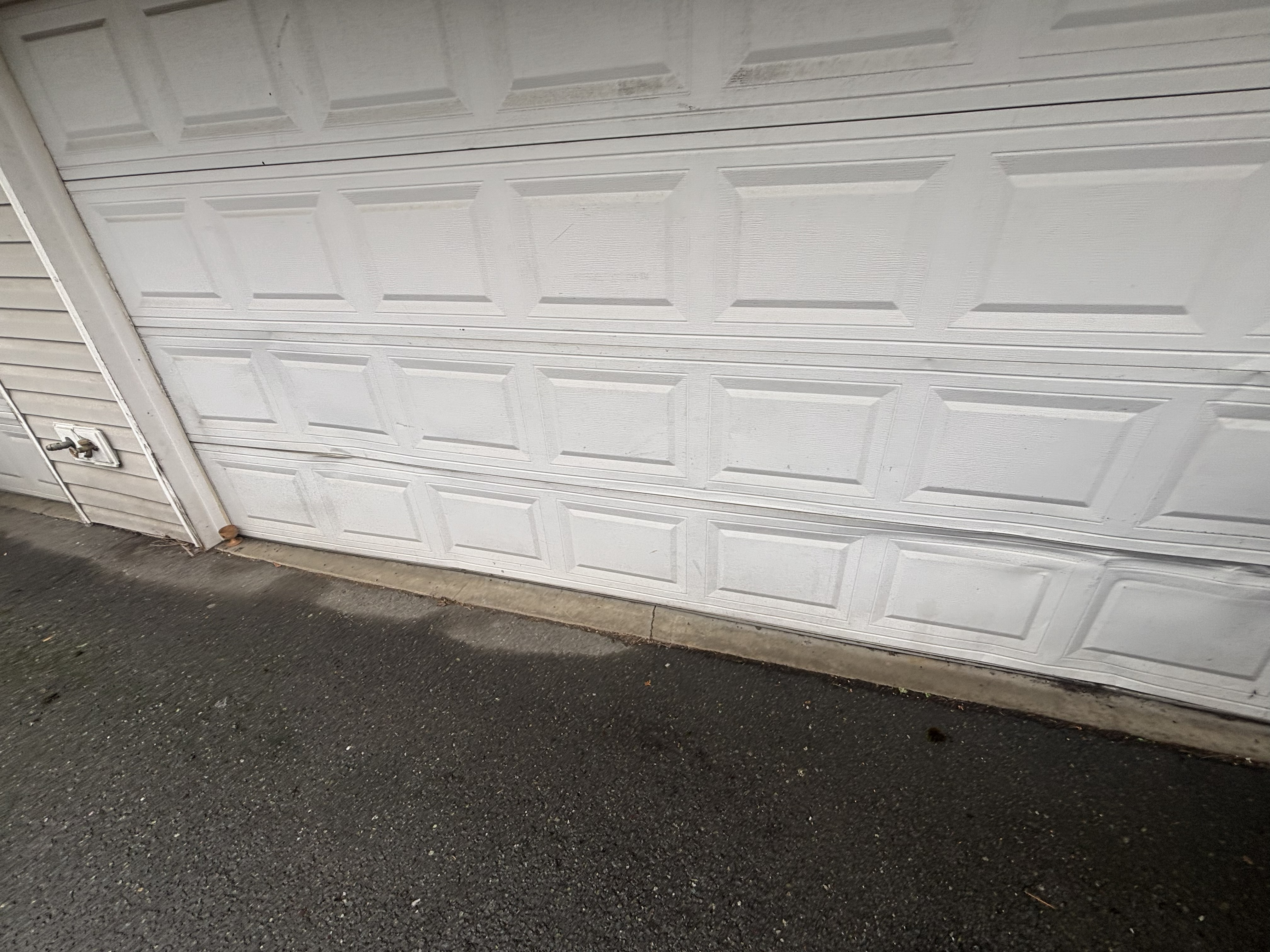 Bottom edge of a white raised-panel garage door meeting a concrete sill and driveway
