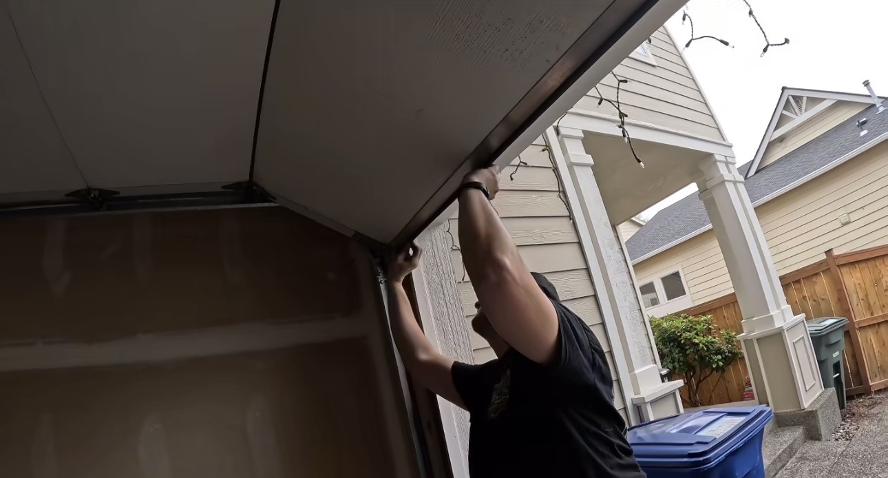 Wesley Zietz reaching up to work along the edge of an open garage door.
