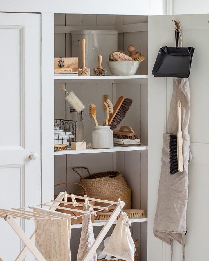Placard de rangement complet avec brosses, panier tressé, pelle noire suspendue et tablier en lin – univers ménage naturel Iris Hantverk Les Jolies Emplettes