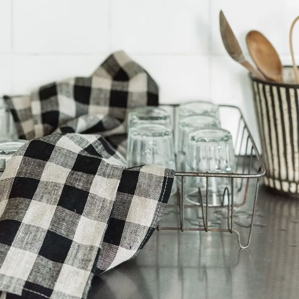 Torchon en lin à carreaux noir et blanc posé sur un égouttoir avec verres et ustensiles en bois – linge de cuisine naturel Les Jolies Emplettes
