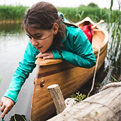 Una niña en un bote de madera toca el agua de un lago
