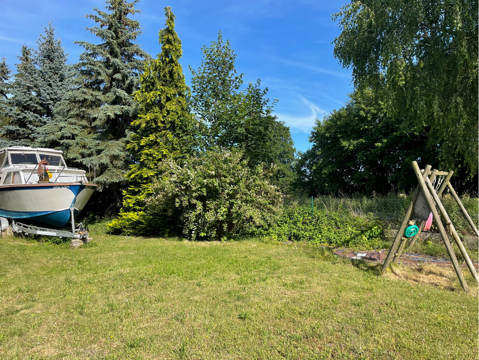 Zweifamilienhaus in Nauen zum Verkauf: Großer, sonniger Garten mit weiter Rasenfläche, Schaukelgerüst für Kinder und dichter, grüner Bepflanzung im Hintergrund.