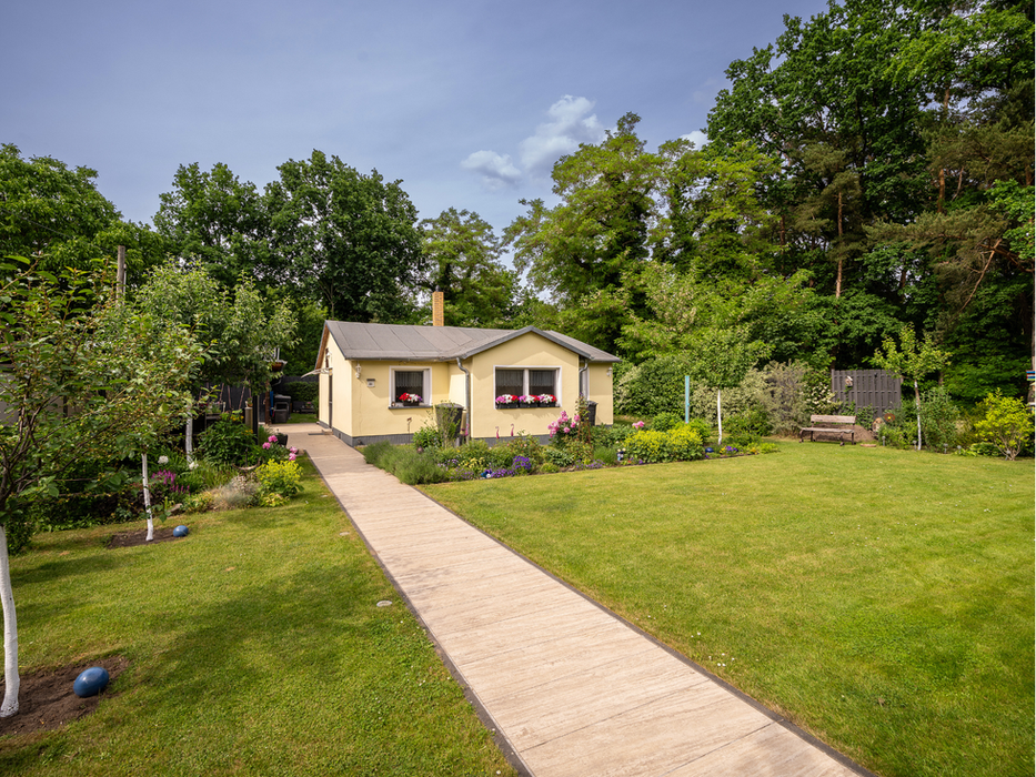 Kaufangebot: Außenansicht des gelben Nebenhauses in Petershagen/Eggersdorf mit gepflegtem Garten, angelegtem Gehweg und umliegenden Bäumen.