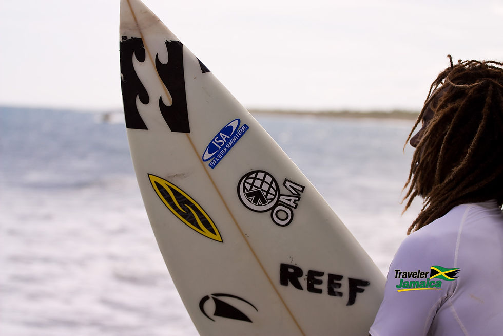 A surfer with dreadlocks gazes at the ocean, holding a sticker-adorned surfboard, ready to embrace the waves of Jamaica.