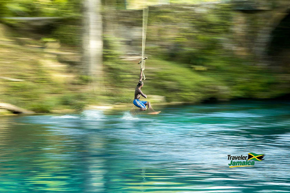 Man in blue shorts zip-lining over a turquoise river in a lush forest, splashing water; Traveler Jamaica logo.