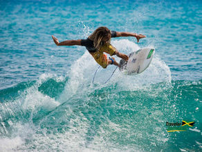 A surfer at Makka Pro Surf competition Jamaica expertly executes an aerial maneuver, soaring above the vibrant turquoise waves with precision and style.