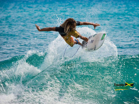 A surfer at Makka Pro Surf competition Jamaica expertly executes an aerial maneuver, soaring above the vibrant turquoise waves with precision and style.