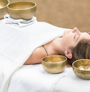 Young woman laying on a massage bed with tibetan singing bowl outdoor. Nepal copper singin