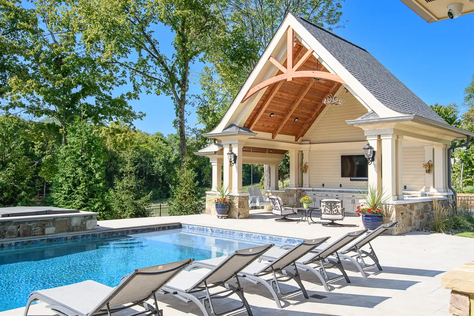 Luxury pool and pool house in a custom Frazier Home at Triple Crown featuring a resort-style swimming pool, stone patio, lounge seating, and a covered pavilion with vaulted wood ceilings designed for elevated outdoor living.