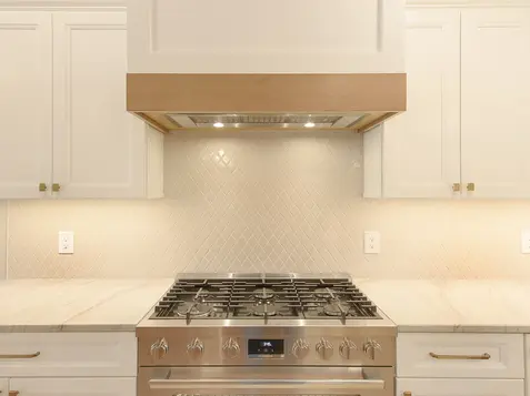 Stainless steel gas range with custom wood-accent hood and white cabinets in a luxury Montgomery kitchen remodel.