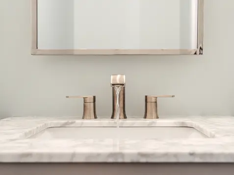 Polished nickel sink fixture with running water above a marble vanity and gray cabinetry in a custom Frazier Homes bathroom.