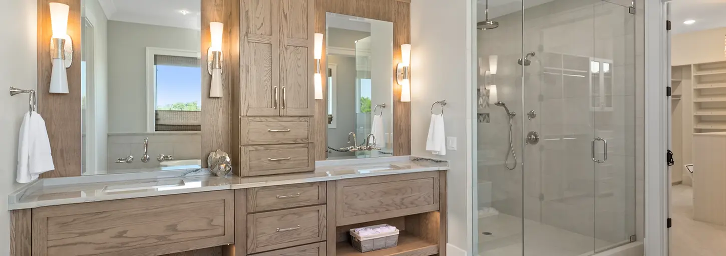 Luxury primary bathroom featuring dual wood vanities with quartz countertops, modern sconces, and a frameless glass walk-in shower designed by Frazier Homes in Cincinnati.