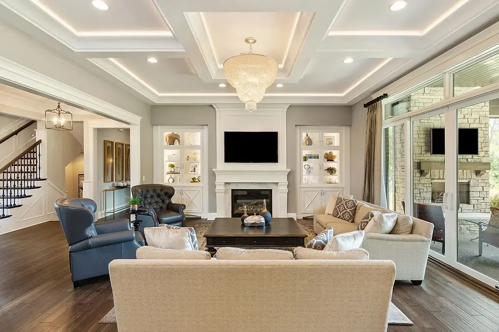 Luxury custom home living room with a coffered ceiling, chandelier, built-in shelving, fireplace, and open layout showcasing refined architectural details.