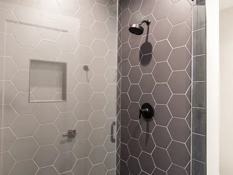 Modern shower with large hexagon wall tile, matte black shower fixtures, frameless glass enclosure, and contrasting grid tile floor in a luxury Frazier Homes Walworth Junction property.