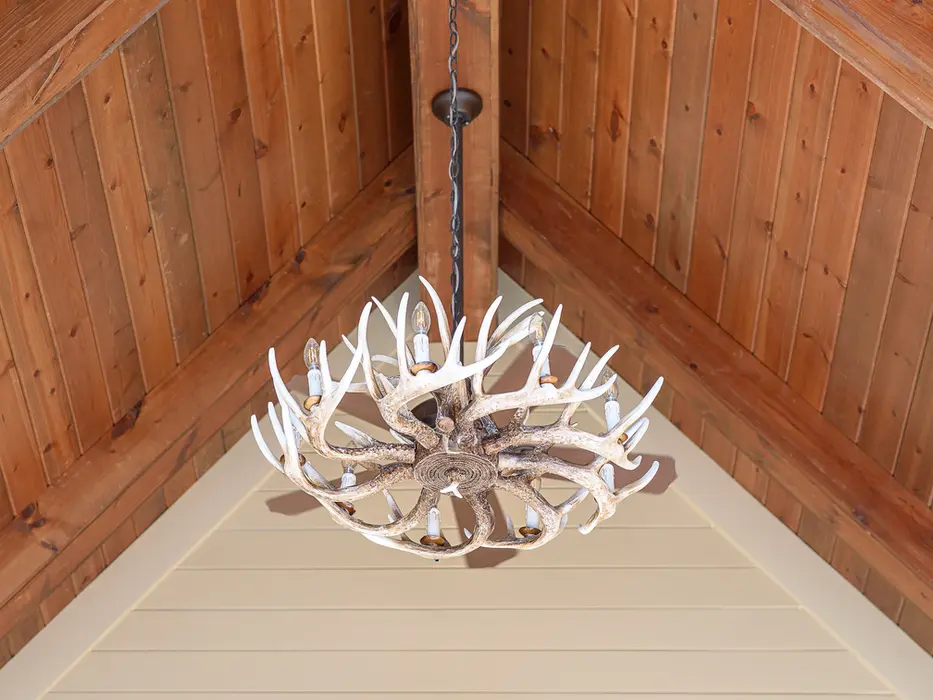 Antler chandelier hanging from a wood-beam ceiling in a covered outdoor living pavilion at a luxury custom home in Triple Crown, Kentucky by Frazier Homes.