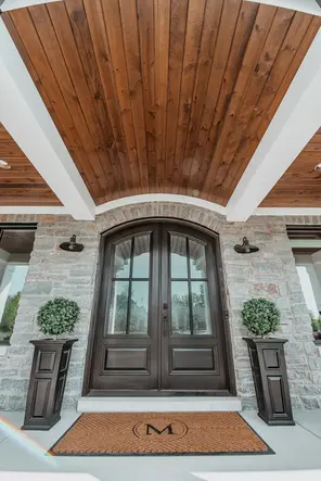 Elegant custom home entryway in Mason, Ohio built by Frazier Homes, featuring a double arched front door, natural stone exterior, and wood-paneled ceiling with timeless architectural detailing.