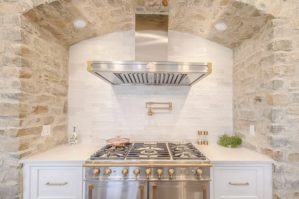 Luxury custom kitchen by Frazier Homes featuring a professional gas range, stone arch surround, white tile backsplash, and gold-accented fixtures, showcasing craftsmanship and attention to detail by an experienced general contractor.