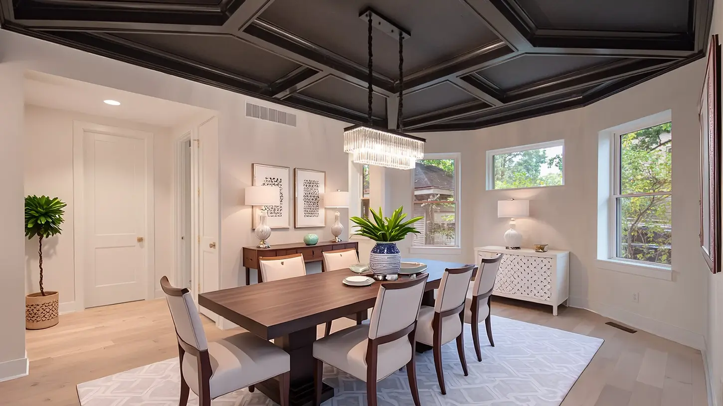 Hyde Park dining room remodel by Frazier Homes featuring a dark coffered ceiling, modern crystal chandelier, walnut dining table, upholstered chairs, light hardwood floors, and large windows overlooking mature landscaping.
