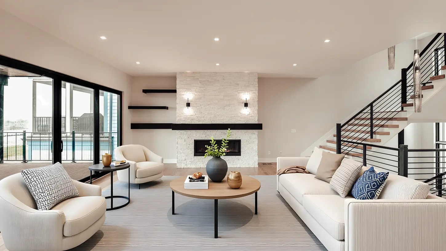 Luxury modern living room in Walworth Junction built by Frazier Homes featuring wide-plank hardwood flooring, custom stone fireplace, floating shelves, modern staircase, and expansive sliding glass doors.