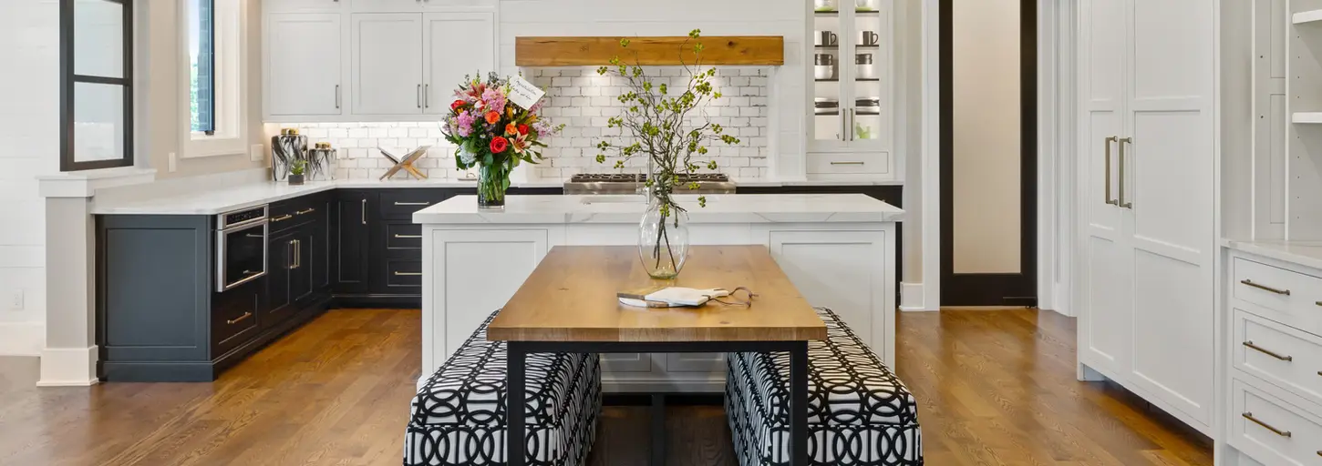 A modern white kitchen with luxurious appliances and a breakfast area featuring a table with black and white benches. This award-winning design combines functionality with elegant aesthetics.