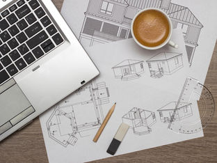 Architectural blueprints and custom home design drawings on a desk with planning tools, illustrating early-stage planning for new construction homes by Frazier Homes.