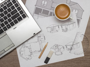 Architectural blueprints and custom home design drawings on a desk with planning tools, illustrating early-stage planning for new construction homes by Frazier Homes.