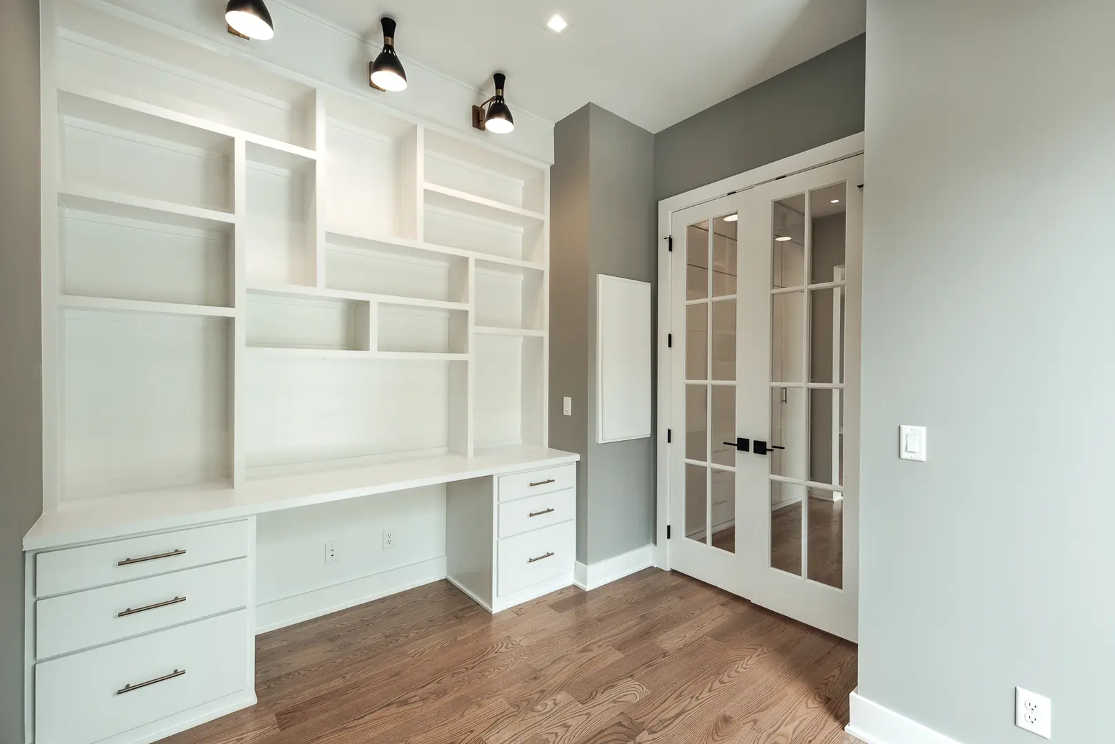 Custom built-in white cabinetry and shelving in a modern Walworth Junction home office with glass French doors and hardwood floors.