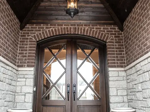 Custom arched wood double front doors with diamond glass, brick and stone entryway, and cedar barrel ceiling by Frazier Homes.