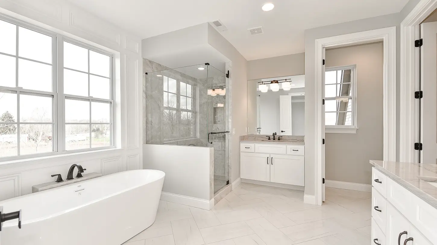 Luxury Liberty Township master bathroom with freestanding tub, glass shower, herringbone tile floors, and custom white cabinetry by Frazier Homes