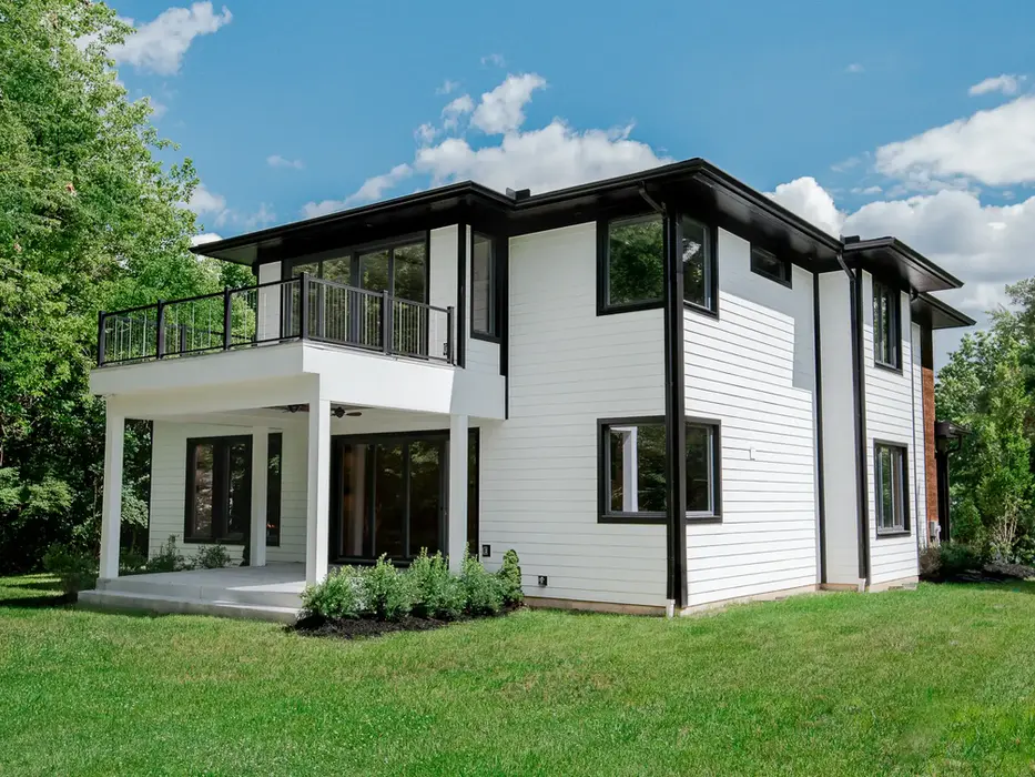 Modern custom home in Montgomery, Ohio featuring white siding, black trim, covered patio, second-story balcony, and private backyard by Frazier Homes.