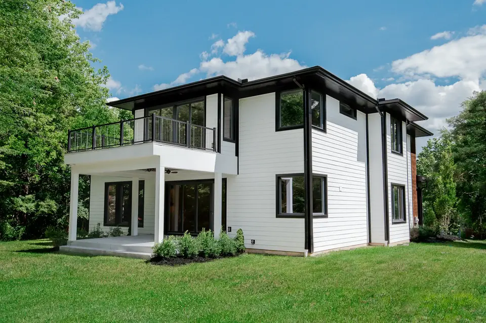 Modern custom home in Montgomery, Ohio featuring white siding, black trim, covered patio, second-story balcony, and private backyard by Frazier Homes.