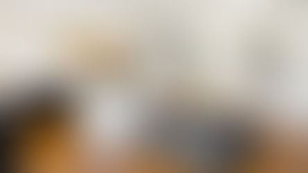 Bright, custom-designed kitchen featuring white cabinetry, a white island with marble countertop, integrated bench seating with patterned upholstery, a built-in wood dining table, dark lower cabinets, a stainless steel range, and a rustic wood hood surrounded by white shiplap and subway tile backsplash.