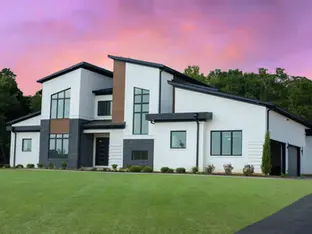 Modern custom luxury home by Frazier Homes featuring white brick, dark stone accents, and expansive architectural windows under a vibrant sunset sky.