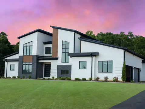 Modern custom luxury home by Frazier Homes featuring white brick, dark stone accents, and expansive architectural windows under a vibrant sunset sky.