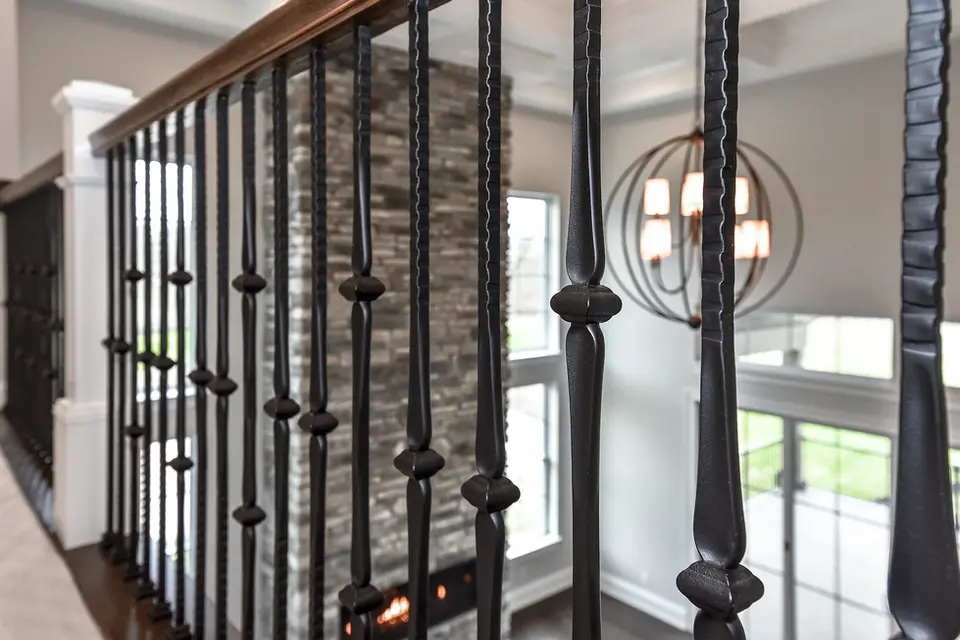 Close-up of custom wrought iron stair railing in a Liberty Township, Ohio luxury home featuring hardwood handrail, two-story great room, floor-to-ceiling stone fireplace, and designer chandelier by Frazier Homes.